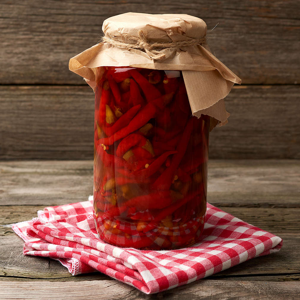 glass jar with pickled rolled up red chili peppers on a wooden background, close up