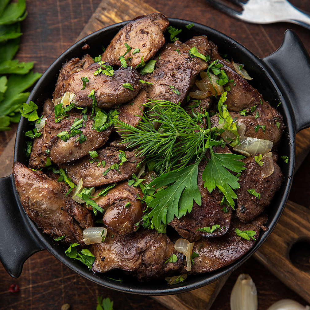 fried chicken liver in black pot, wooden background, top view