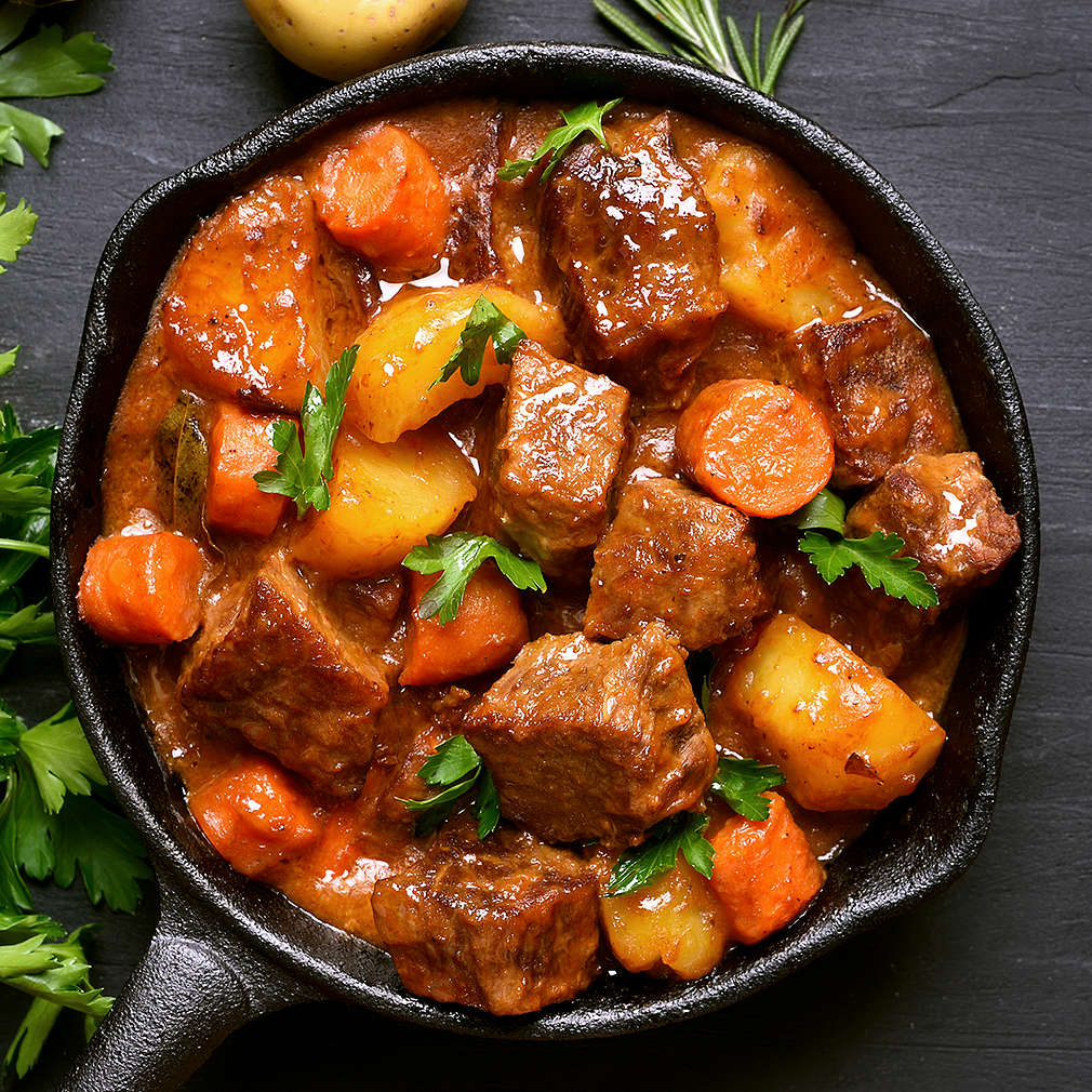 Beef stew with potatoes, carrots and herbs on black background with copy space, top view