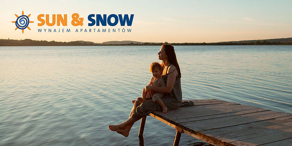 Kobieta z małym dzieckiem na rękach siedzi na molo nad wodą