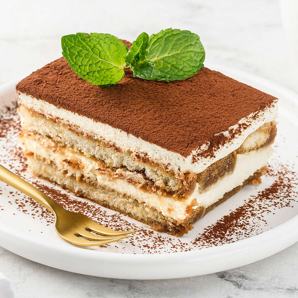 Traditional italian dessert tiramisu on a white plate on a marble table. Close-up. Selective focus