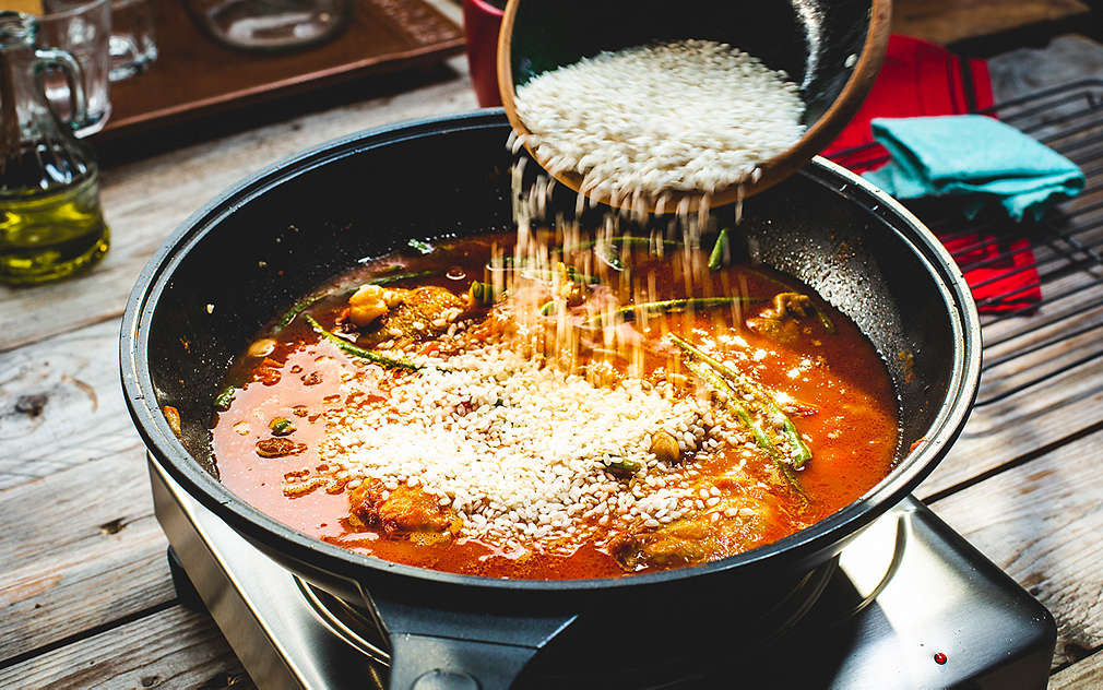 Osoba dodaje rižu u tavu s paellom.