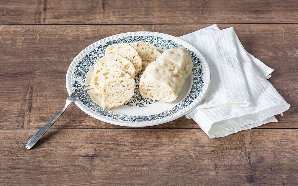 Dwa pokrojone czeskie knedle leżą na talerzu, obok nich widelec.