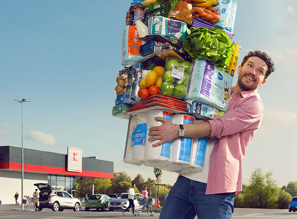 Man carrying many Kaufland products stacked on top of each other 