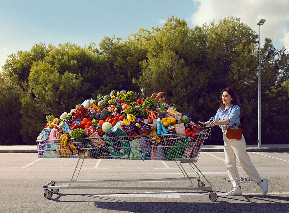 Woman pushing an oversized shopping cart in front of her, which is packed with various Kaufland products.
