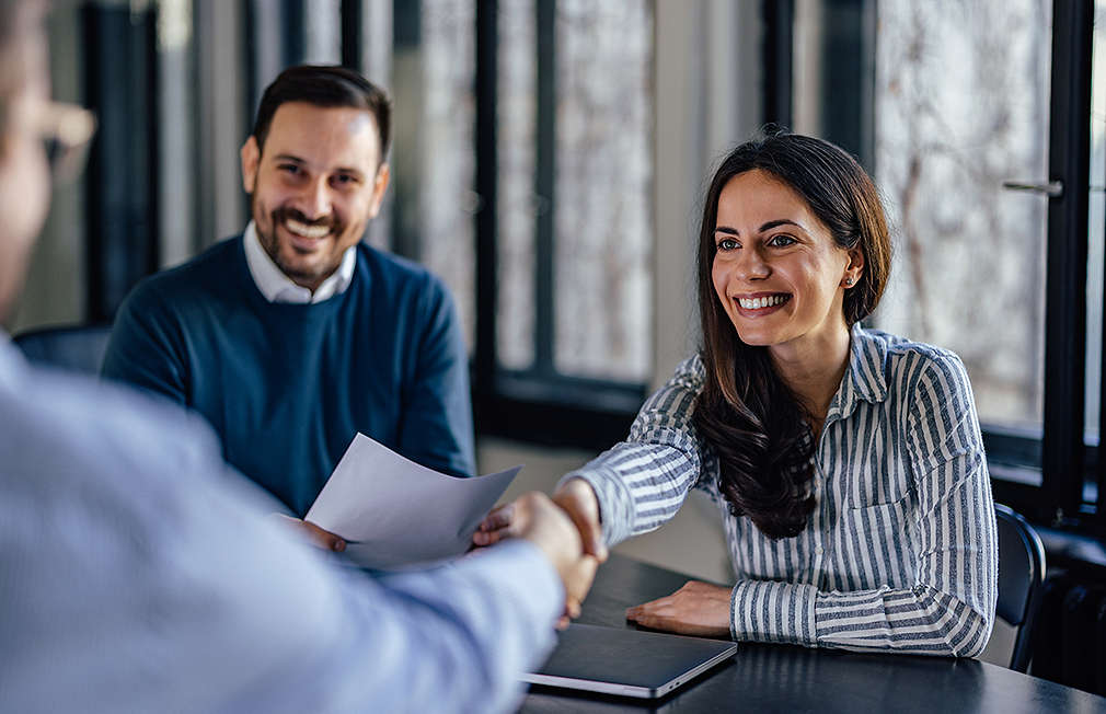 A man and a woman are talking to another person. The woman shakes this person's hand.