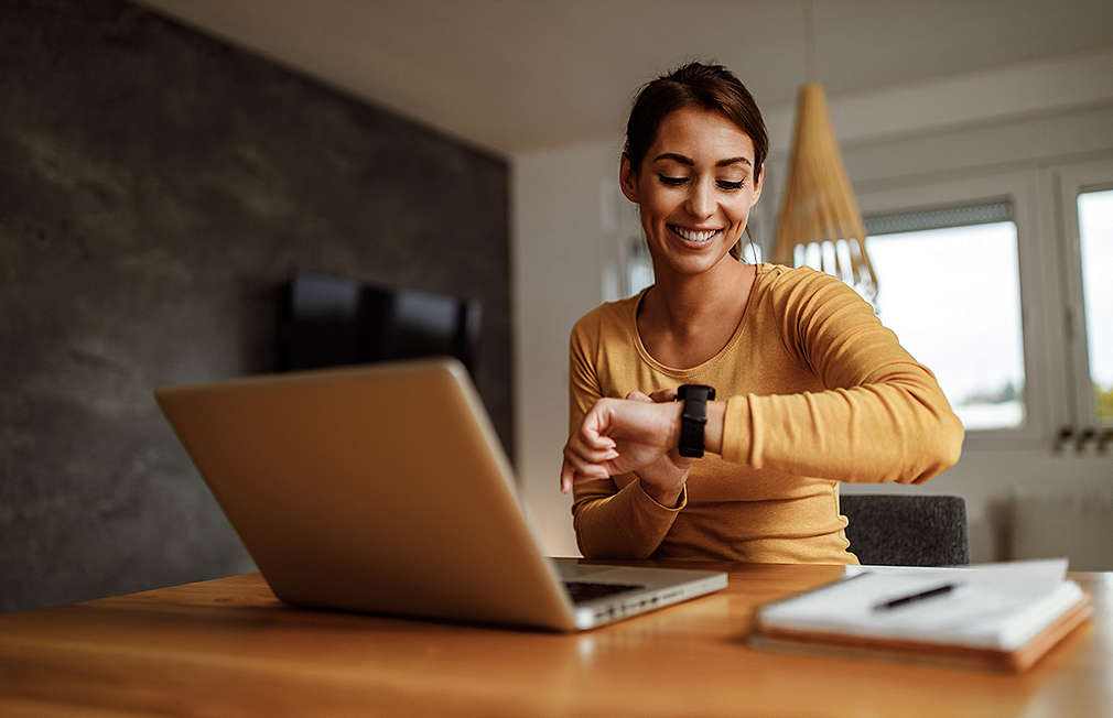 Woman sitting in front of a laptop and looking at her watch