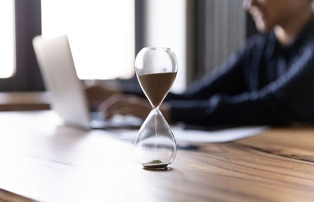 Person sits in front of laptop, in front of it is an hourglass