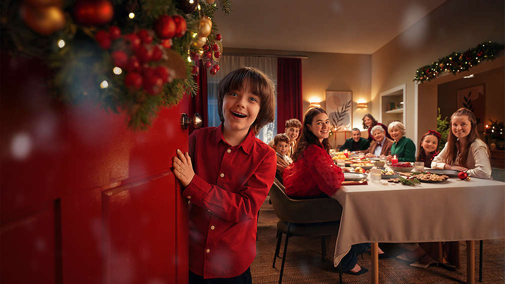 Junge, der die Tür begeistert öffnet; Familie am Esstisch im Hintergrund