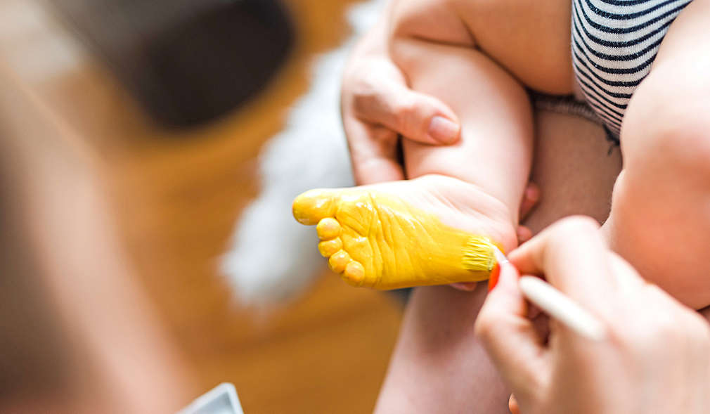 Babyfuß wird für Abdruck Fuß mit gelber Farbe angemalt