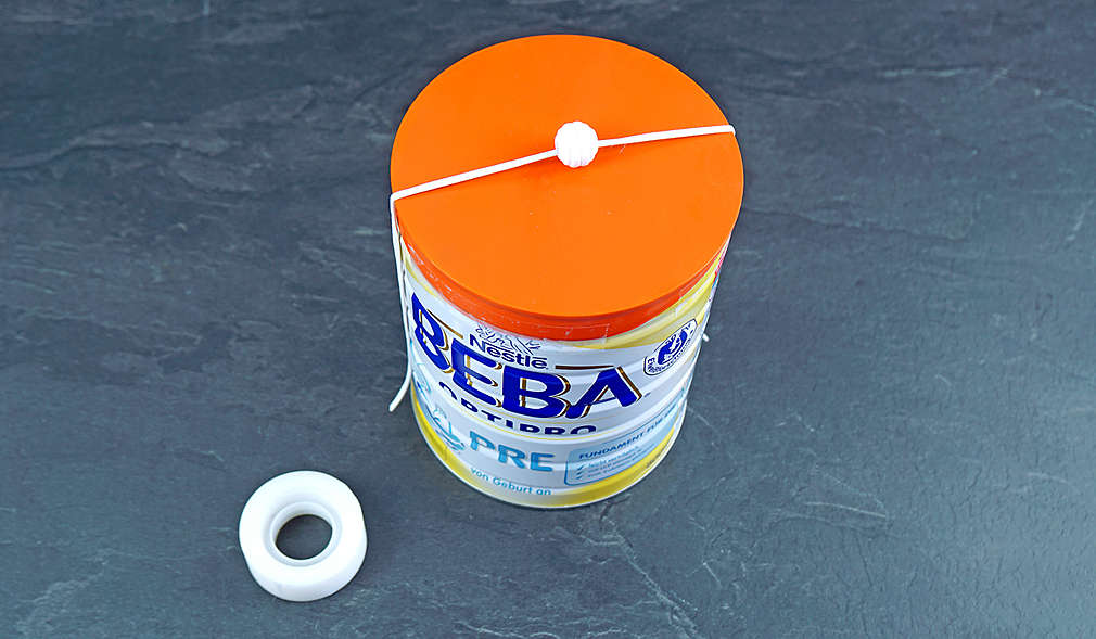 Abbildung: Klebebandrolle und Folgemilch-Dose mit Gummiband