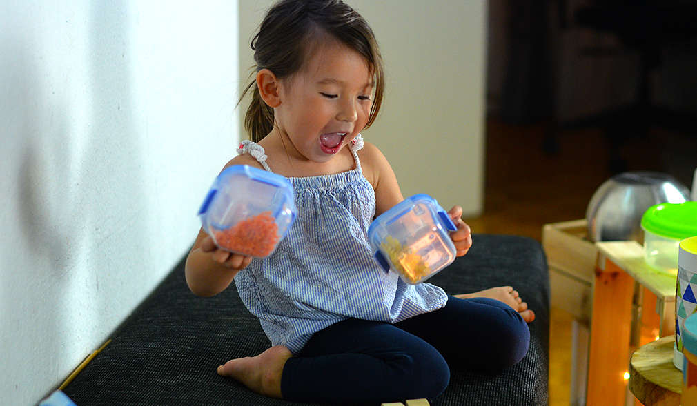 Kleines Mädchen schüttelt zwei Plastikdosen mit Inhalt