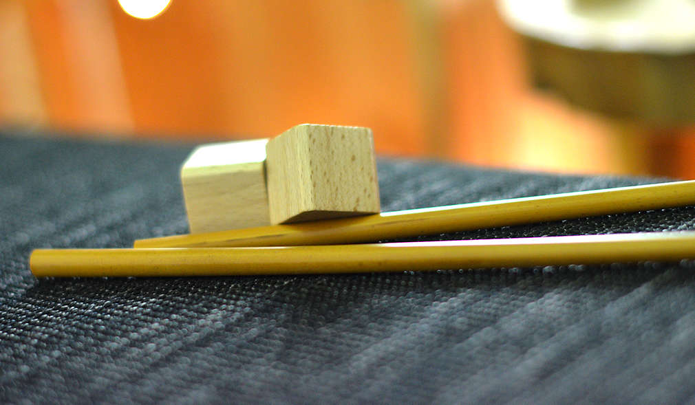 Zwei Essstäbchen liegend, darauf zwei kleine Holzklötze in Würfelform