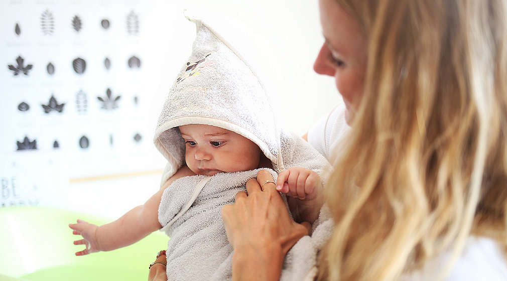 Mama wickelt Baby in Kapuzenhandtuch ein