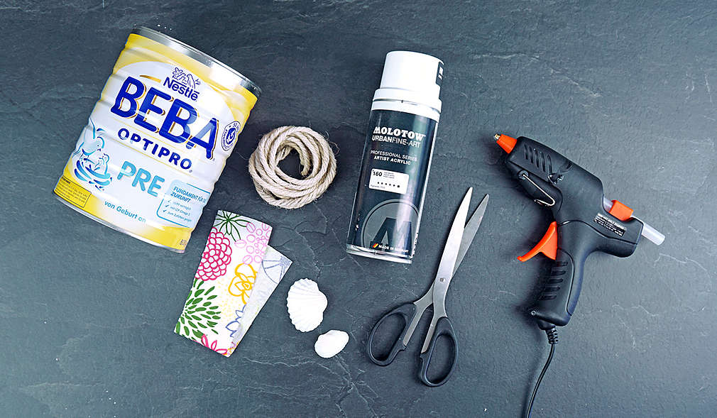 Dose Nestlé BEBA Pre- oder Folgenahrung, weißer Acryl-Sprühlack, Dekostoffband, Kordel, Schere, Heißklebepistole, und Muscheln 