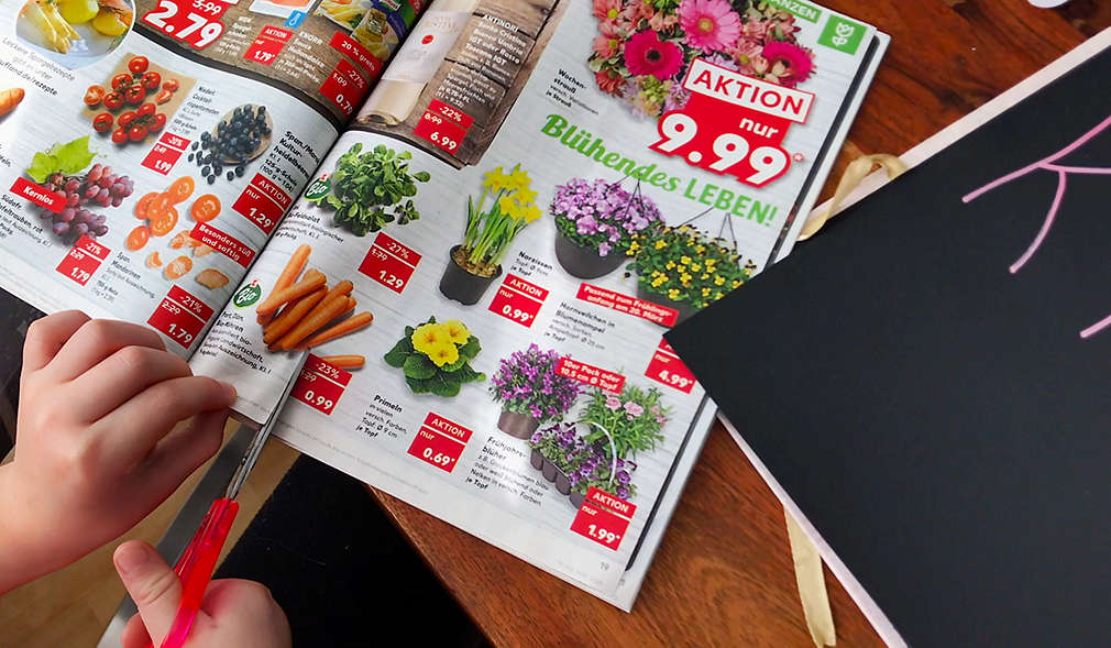 Kind übt das Ausschneiden von Motiven mit einem Werbeprospekt