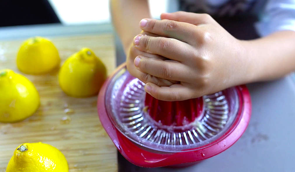 Kind presst mithilfe einer Zitronenpresse frische Zitronen aus