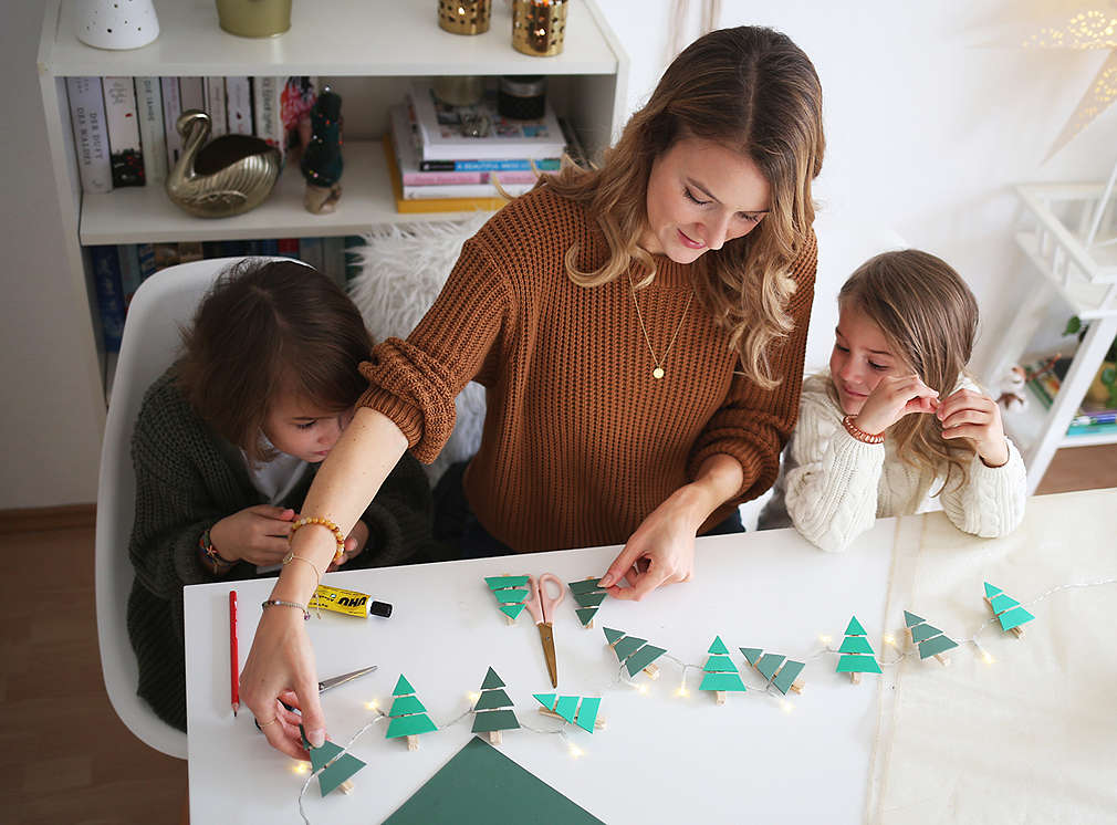 Mutter bastelt mit ihren Kindern eine Weihnachtsbaum-Lichterkette