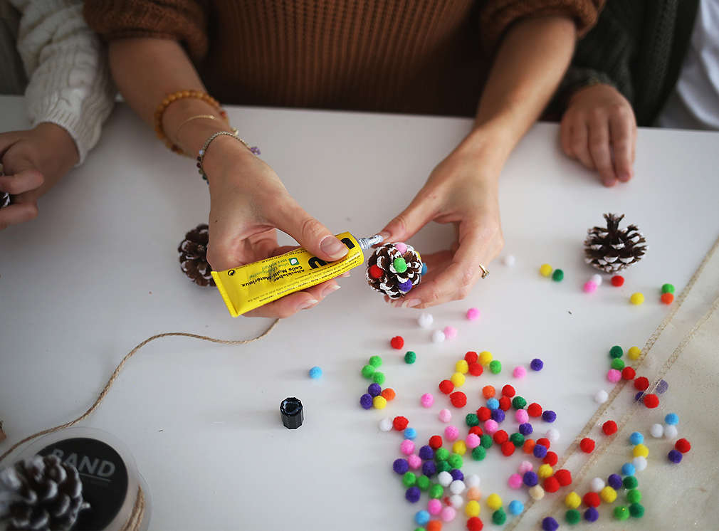 Ein Tannenzapfen wird mit bunten Kugeln beklebt