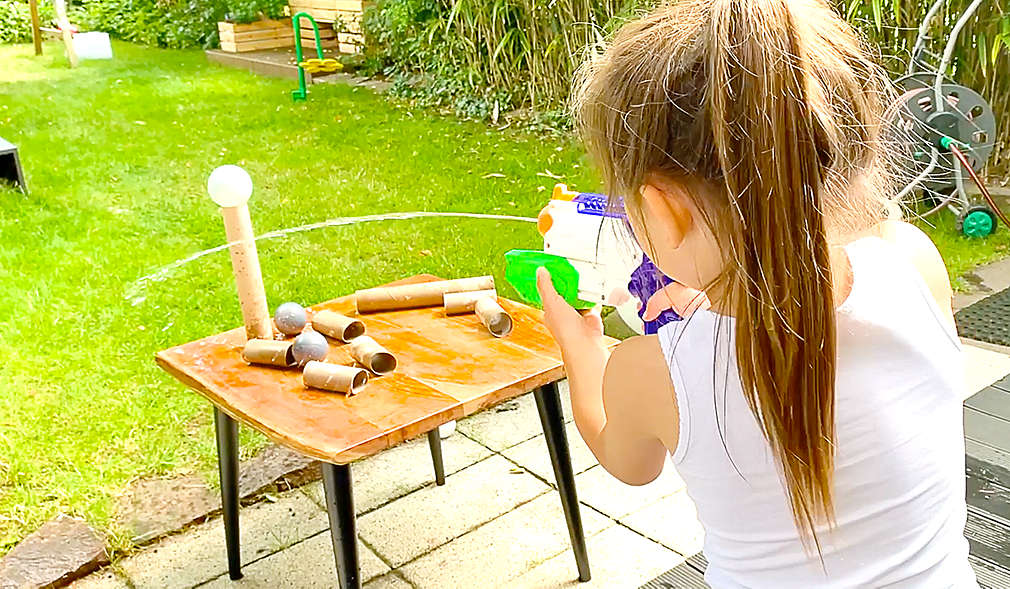 Mädchen schießt mit Wasserpistole auf Bälle