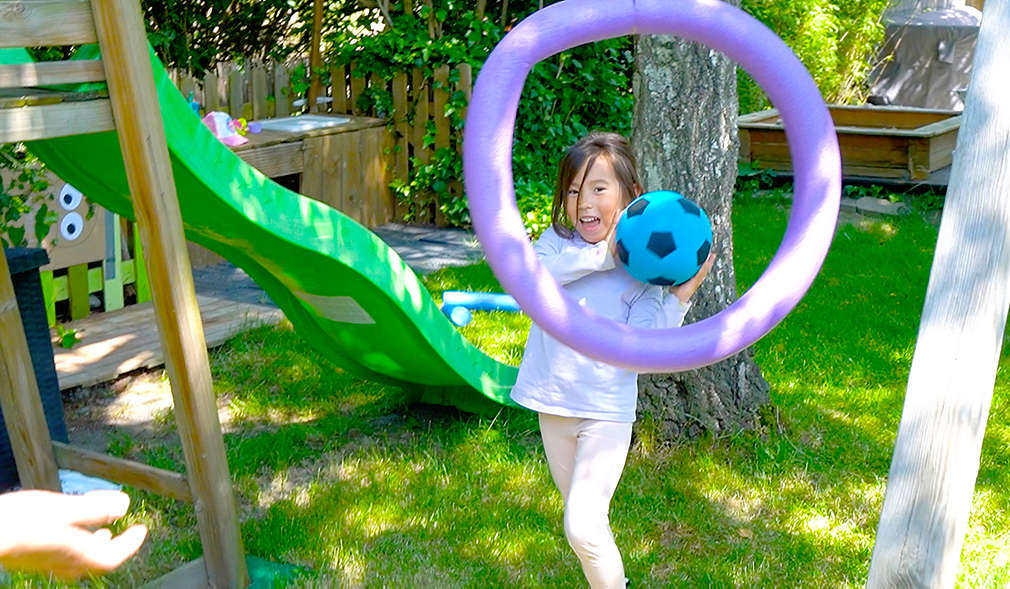 Mädchen wirft einen Ball durch einen Ring aus einer Poolnudel