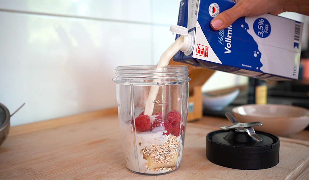 Milch fließt in einen Becher mit Müsli und Obst