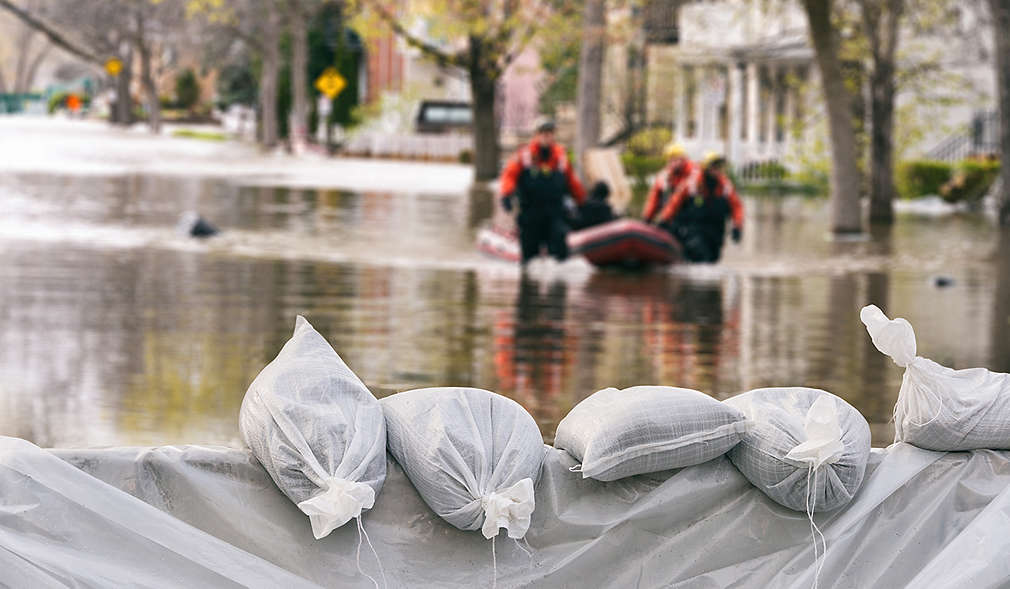 Hochwasser und Helfer mit einem Schlauchboot; Im Vordergrund: Sandsäcke