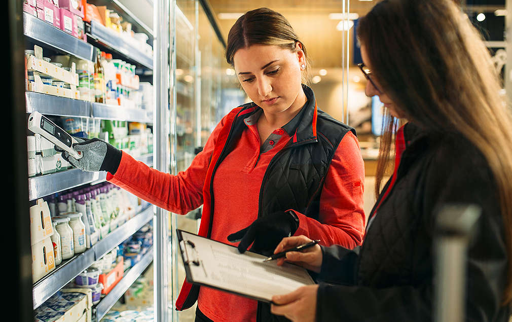 Auszubildende steht mit Kollegin am Molkerei-Produkte-Regal