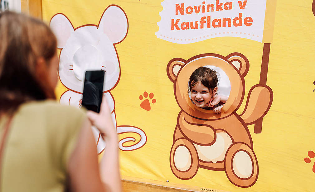 Dievčatko sa usmieva a pózuje s bannerom "Novinka v Kauflande"