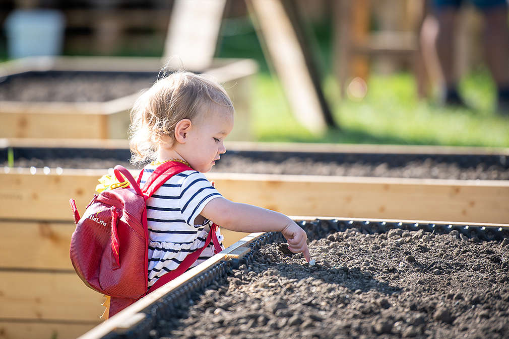 Malé dítě strká prsty do hlíny v záhoně.