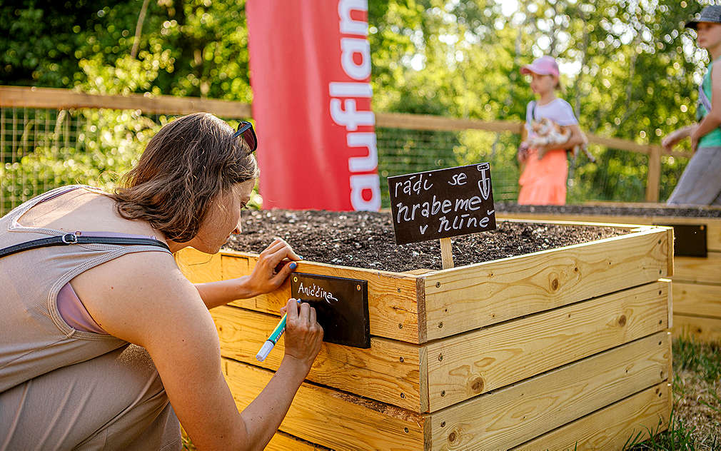 Mladá žena popisuje cedulku na záhoně v komunitní zahradě.