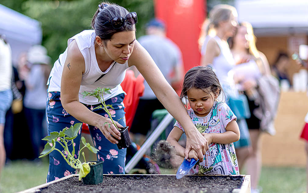 Matka s dcerou sází rostlinky do hlíny.