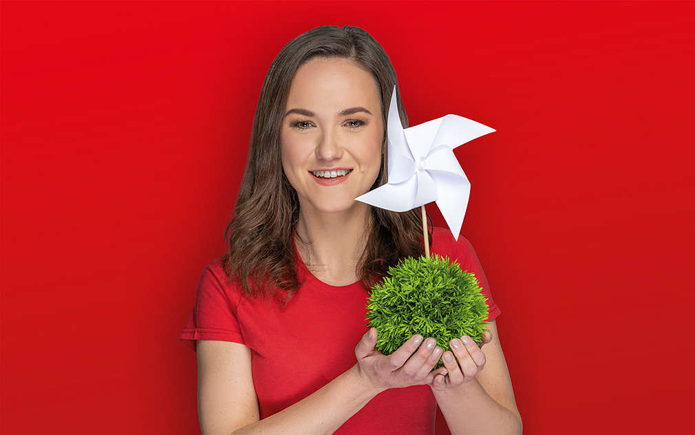 Zaměstnankyně společnosti Kaufland drží v ruce papírový větrník zapíchnutý v mechu