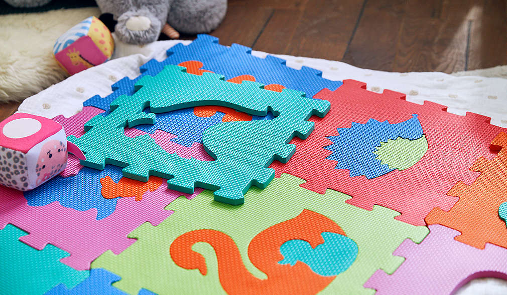 Kind umarmt Kuscheltier und im Hintergrund sitzen weitere Kuscheltiere auf dem Sofa