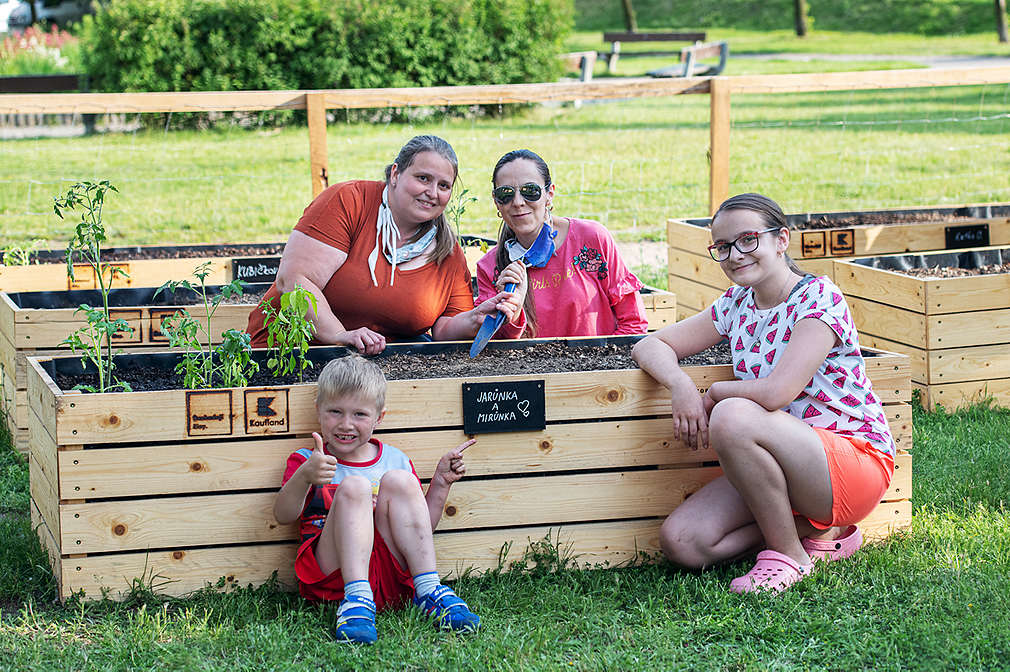 Dvě ženy a dětí sedí u svého záhonu v komunitní zahrádce.