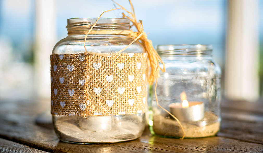 Zwei mit Juteband dekorierte Windlichter stehen auf einem Holztisch