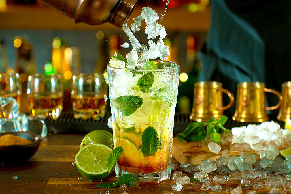 Eine Heimbar, in der ein Cocktail mit Eiswürfeln, Limetten und Minze zubereitet wird