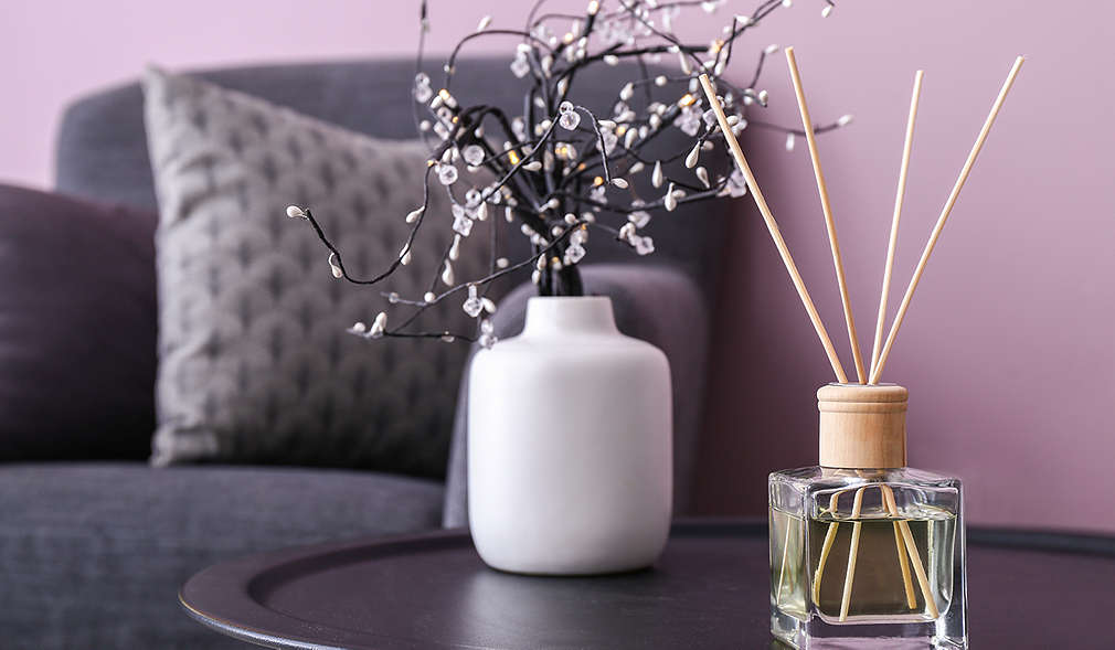 Lavendel-Raumduft auf einem Couchtisch, daneben eine weiße Vase mit einem blühenden Zweig