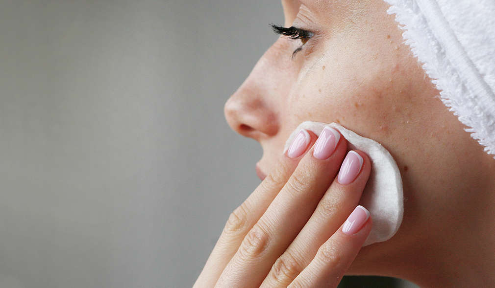 Nahansicht einer Frau, die gerade ihr Gesicht mit einem Wattepad pflegt.