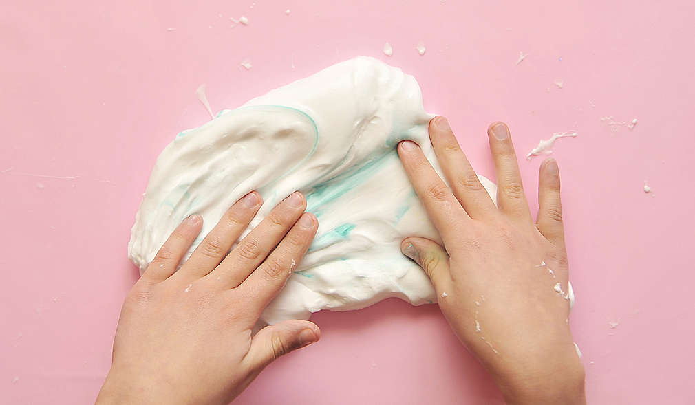 Kinderhände von oben, die eine weiße Masse mit etwas blauer Farbe kneten.