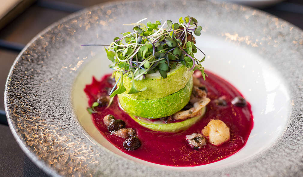 Zucchinischeiben auf einem Soßenspiegel aufgetürmt und mit Sprossen verziert