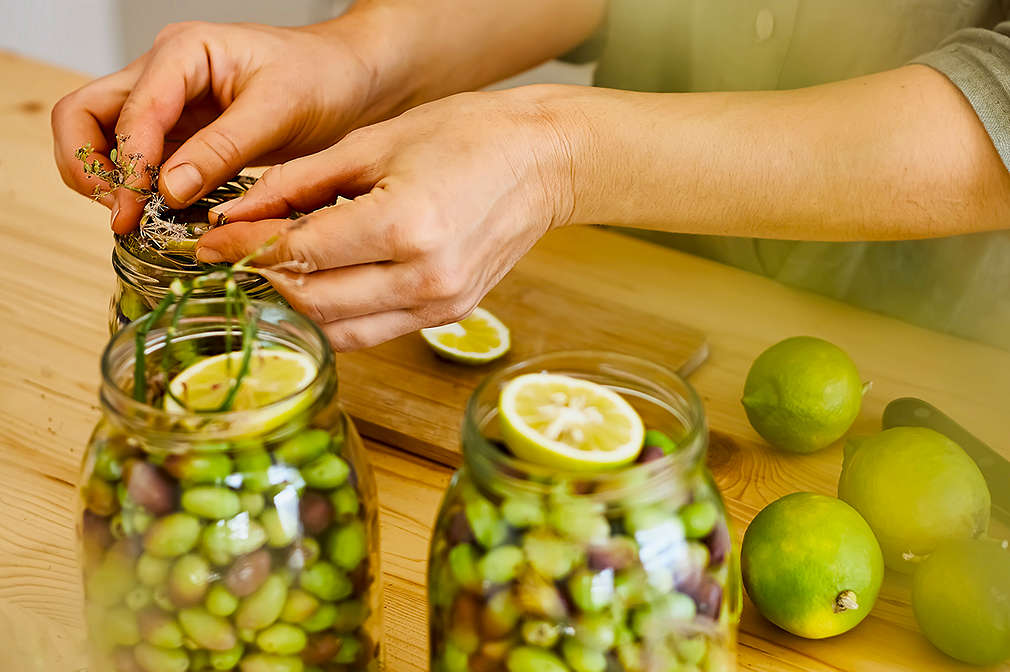 Oliven werden mit einer Zitronenscheibe in einem Bügelglas eingelegt