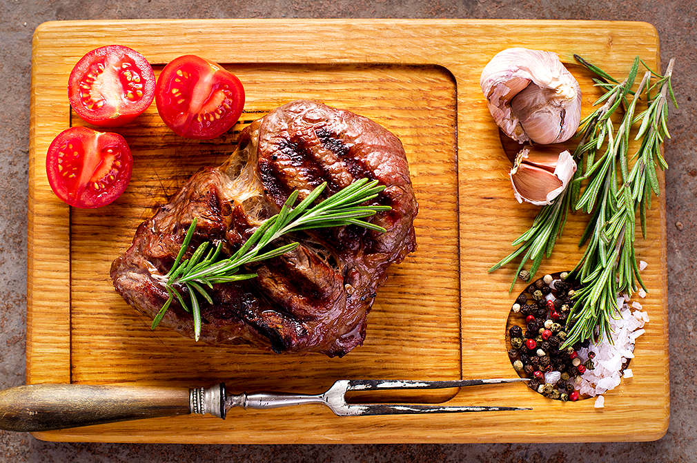 Ein fertiges Steak, Rosmarin und Tomatenschreiben auf einem Holzbrettchen