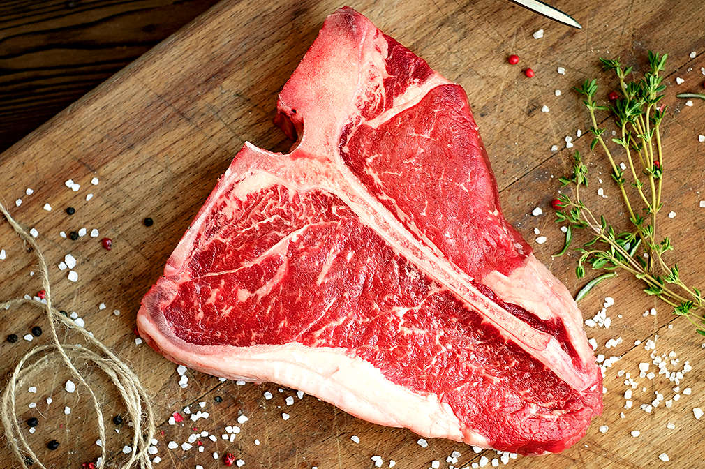 Zu sehen ist ein rohes Stück Fleisch auf einem Holzbrett – mit Salz und anderen Gewürzen