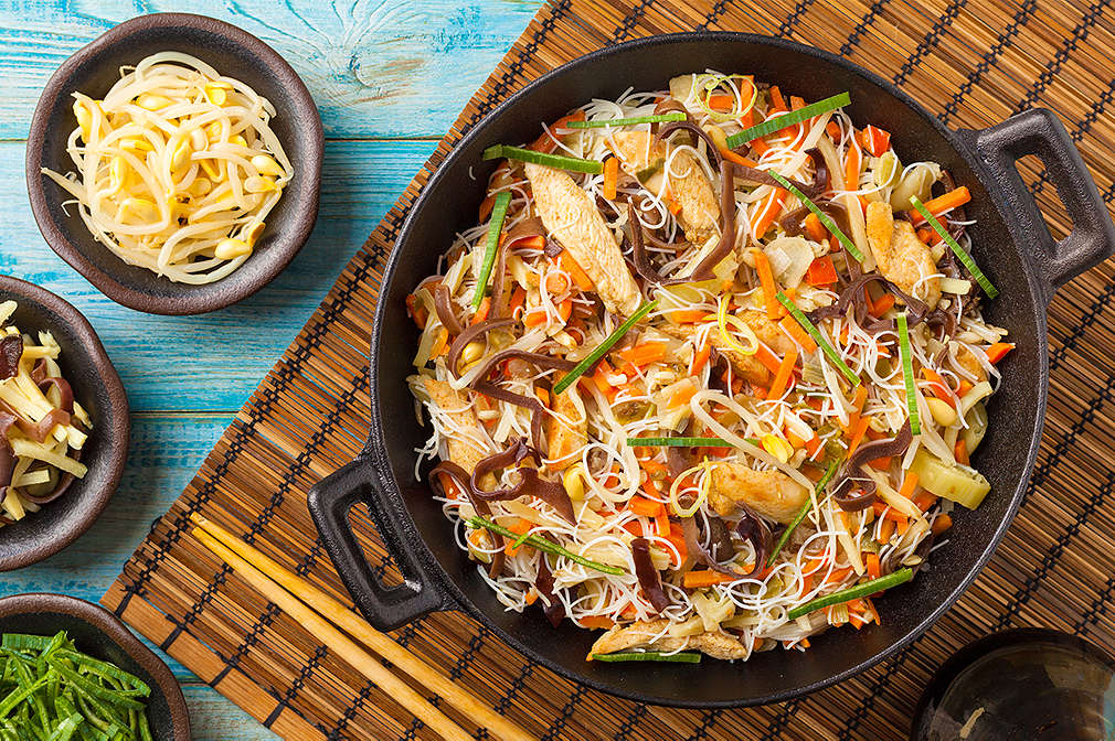 Eine Pfanne mit Asia-Nudeln und kleine Schalen mit verschiedenen Zutaten