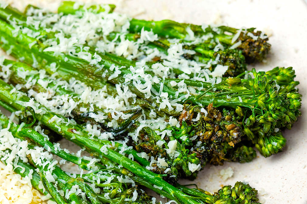 Gerösteter Bimi mit fein geriebenem Parmesan liegt auf einem weißen Teller