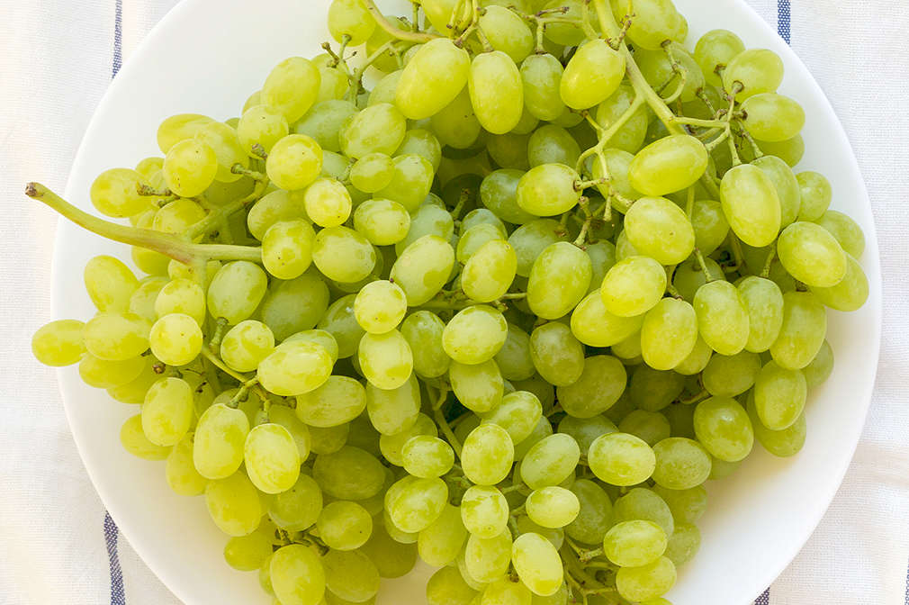 Ein Teller mit Trauben auf einem gestreiften Tischtuch.