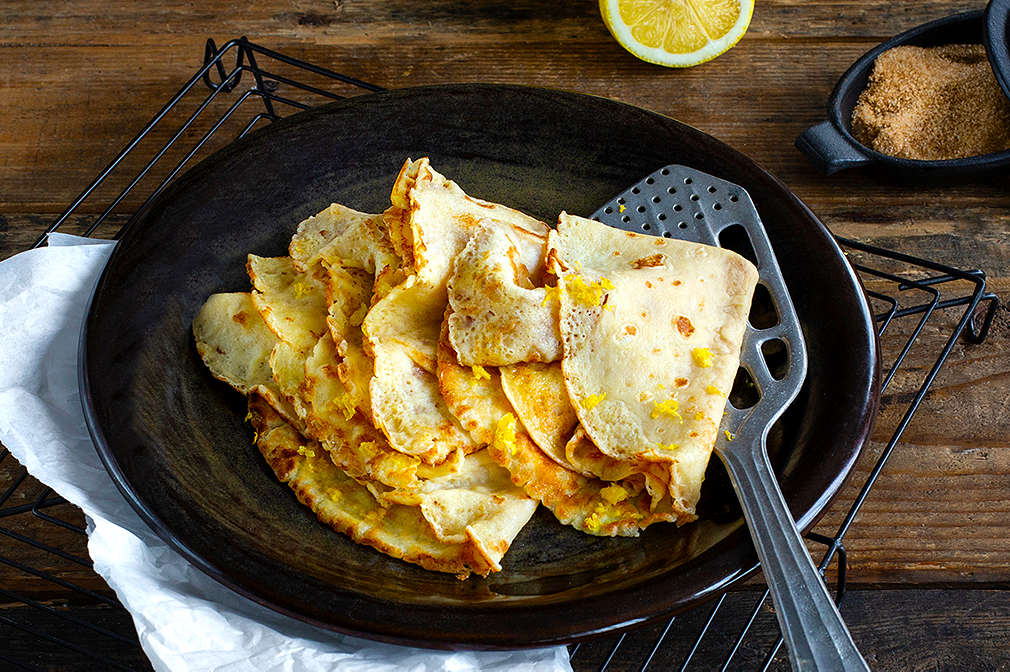 Ein Stapel dünn ausgebackener, zusammengeklappter Crêpes mit Zitronenabrieb auf einem Teller