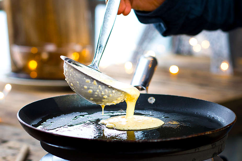 Dünnflüssiger Teig wird mit einer Schöpfkelle in eine flache Pfannkuchenpfanne mit Öl gegeben