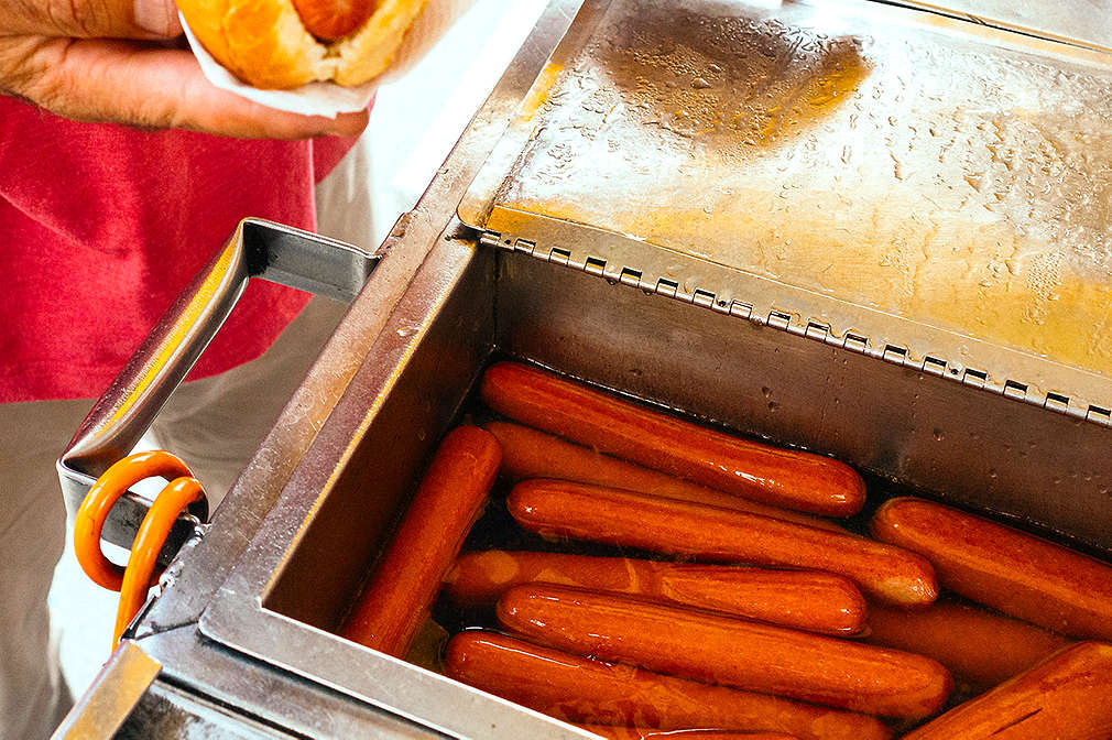 Metallbecken mit in Wasser schwimmenden Brühwürstchen an einem Hot-Dog-Stand